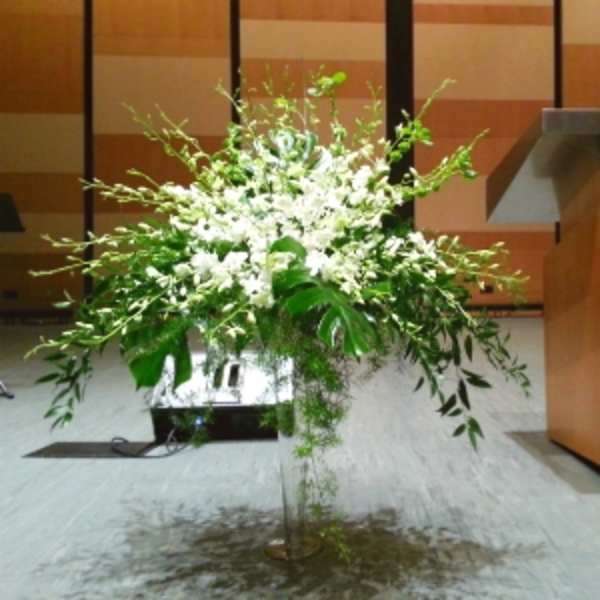 Tall white floral arrangement in a clear vase at a podium