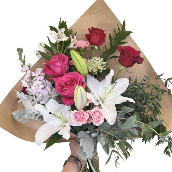 Bouquet of red and pink roses with white lilies and greenery in brown paper