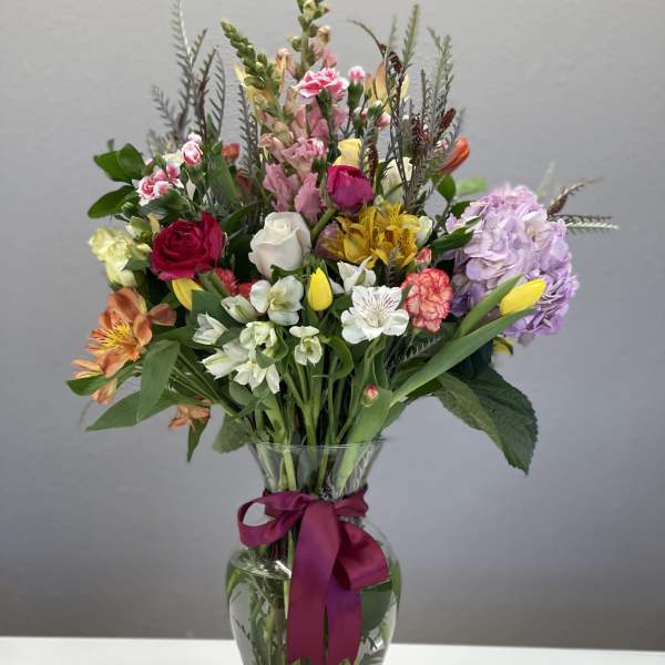 Mixed bouquet in a clear glass vase with a magenta ribbon