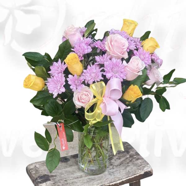 Pink and yellow roses with lavender daisies in a glass vase