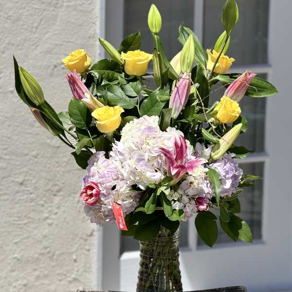Bouquet of yellow roses, pink lilies, and pale hydrangeas in a glass vase