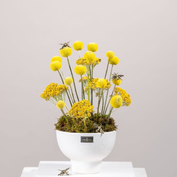 Yellow pom-pom flowers in a white pedestal vase with bee decorations