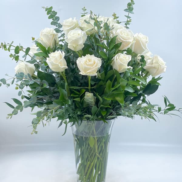 White roses arranged in a clear glass vase with greenery