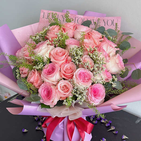 Pink rose bouquet wrapped in lavender paper with a red ribbon