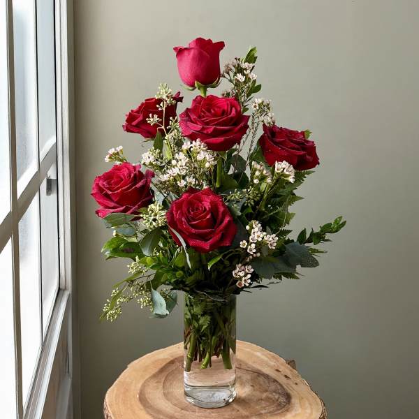 Red roses arranged in a clear glass vase with small white filler flowers.