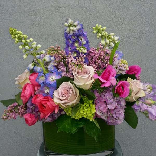Mixed bouquet of roses, hydrangeas, and purple blooms in a glass vase