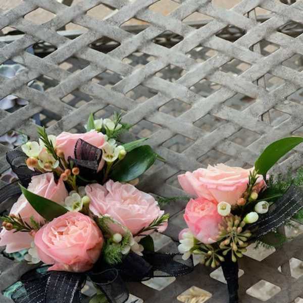 Two small pink rose boutonnieres with black ribbon accents