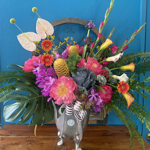 Large tropical floral arrangement in a silver urn with pink, purple, and orange blooms