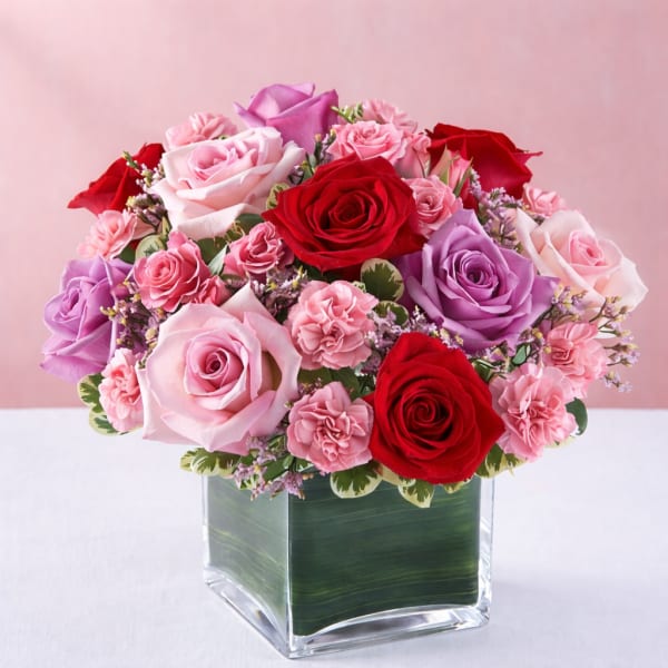 Bouquet of pink, red, and lavender roses in a square glass vase