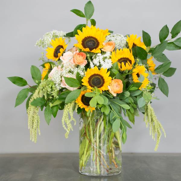 Sunflower and peach rose arrangement in a clear glass vase