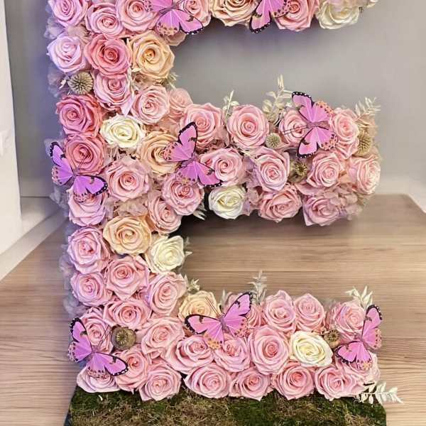 Large floral letter covered in pink and cream roses with butterfly accents