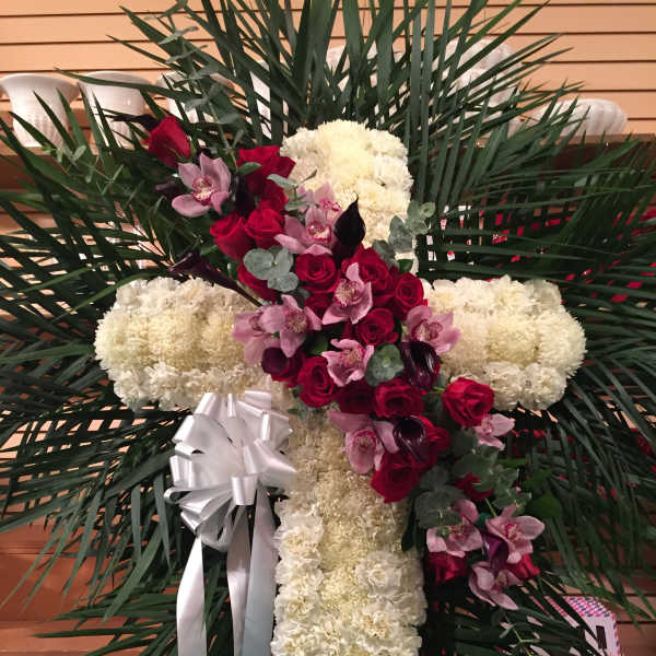 Cross-shaped floral tribute with white carnations, red roses, and pink orchids