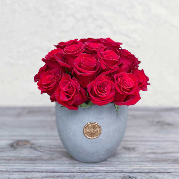 Red roses arranged in a gray vase with a gold emblem