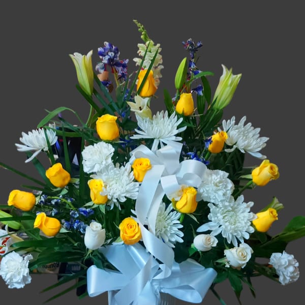 Bouquet of yellow and white flowers in a white vase with a blue ribbon