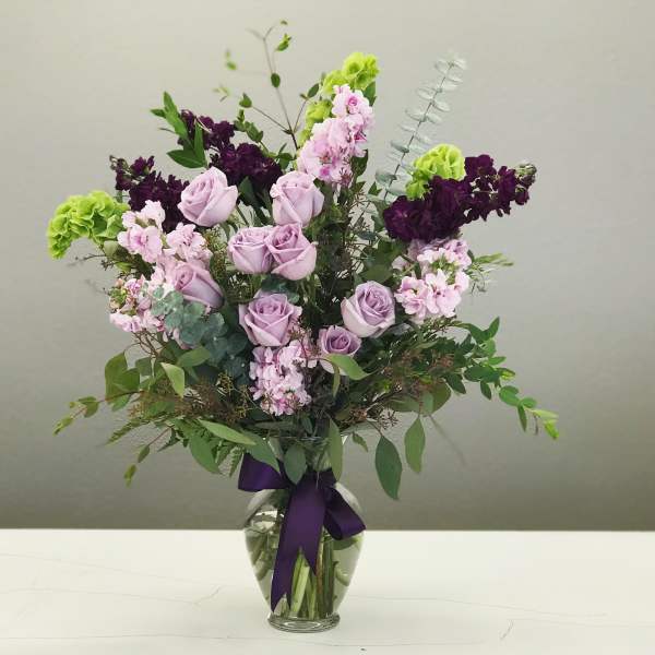 Lavender roses and pink flowers in a glass vase with a purple ribbon