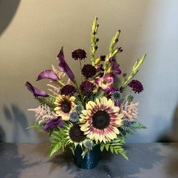 Purple calla lilies and sunflowers in a dark vase