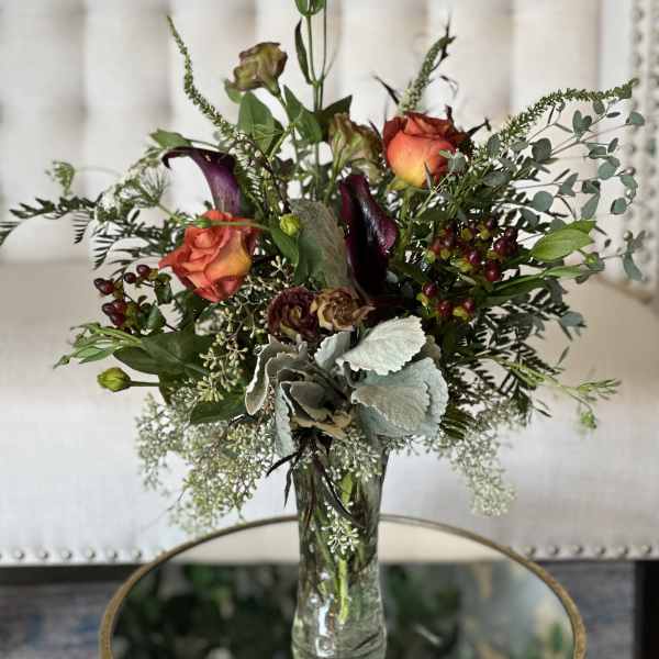 Tall mixed bouquet in a clear glass vase with orange roses and dark calla lilies