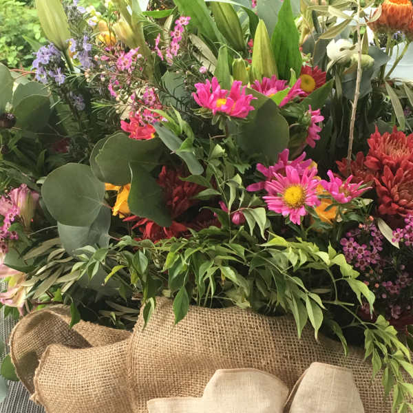 Mixed bouquet with pink and red flowers in burlap wrapping and a large beige bow