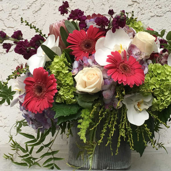 Mixed bouquet with pink gerbera daisies, white orchids, and cream roses in a ribbed vase