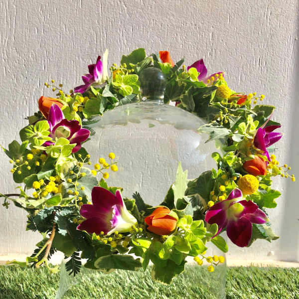 Floral wreath with purple orchids and orange tulips on a glass stand