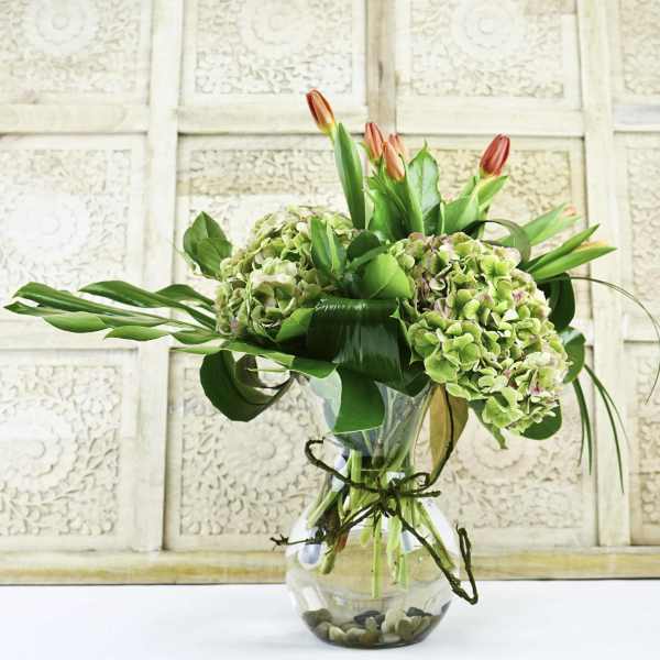 Bouquet of green hydrangeas and orange tulips in a glass vase