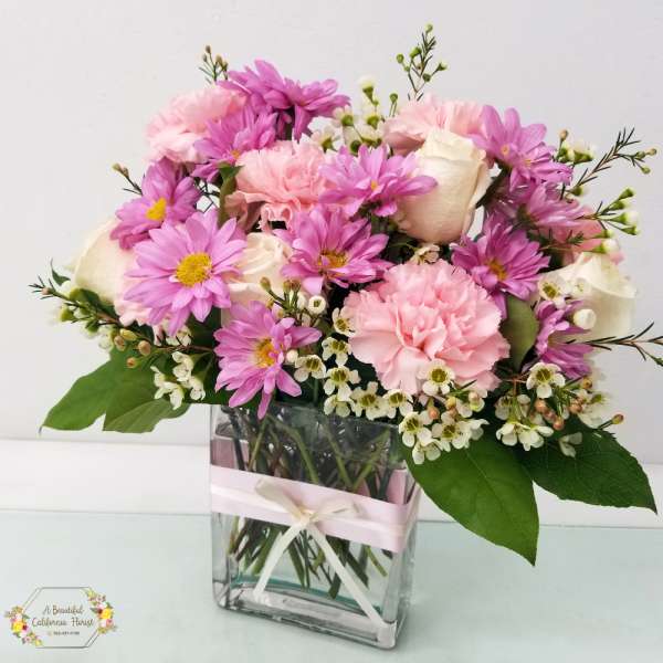 Pink and white bouquet in a clear square vase with a ribbon
