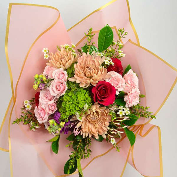 Bouquet of pink and red flowers wrapped in pale pink paper with gold trim