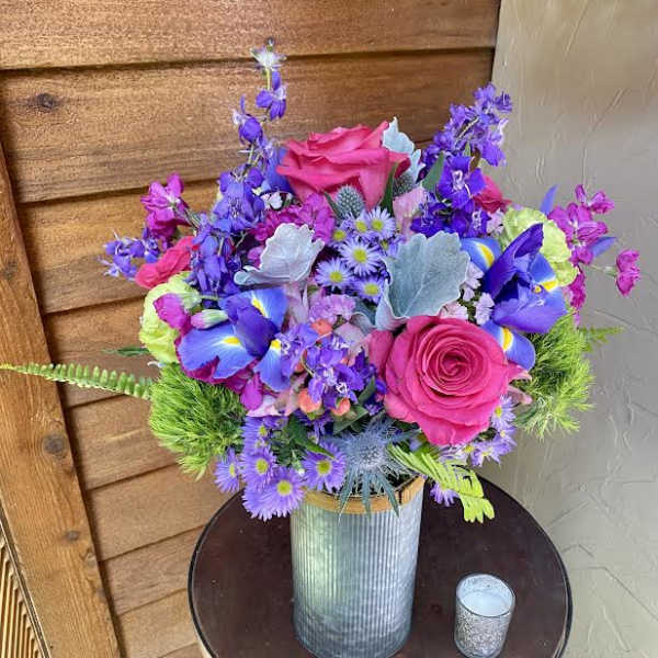 Bright mixed bouquet in a ribbed metal vase with pink roses and purple flowers