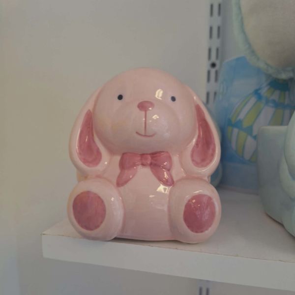 Pink ceramic bunny figurine with a bow sitting on a shelf
