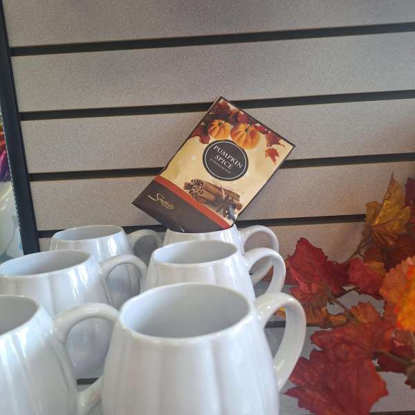 White ceramic mugs displayed with a pumpkin spice sign and autumn leaves.