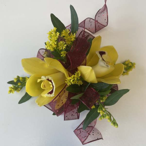 Yellow orchid corsage with burgundy ribbon and greenery