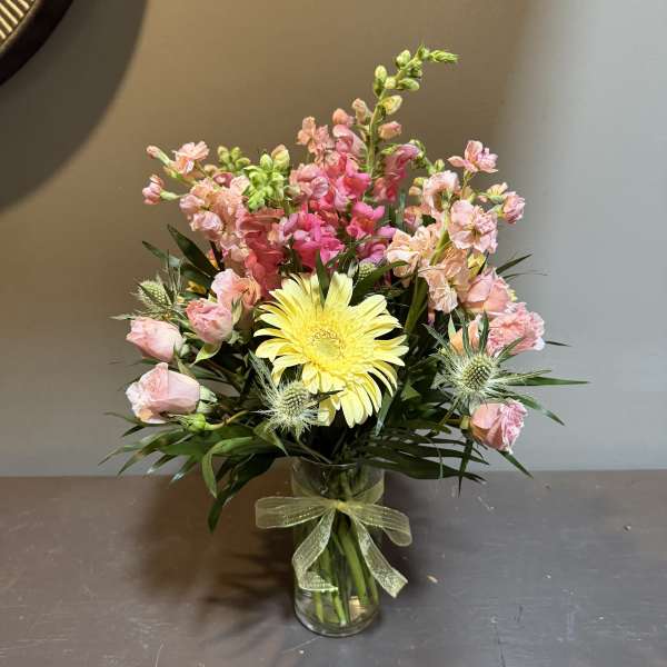 Pink and yellow flower arrangement in a glass vase with a ribbon