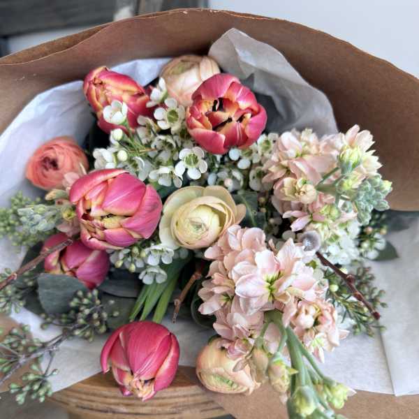 Bouquet of pink tulips and pale flowers wrapped in brown paper