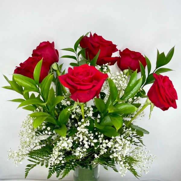 Red roses arranged in a clear glass vase with white filler flowers