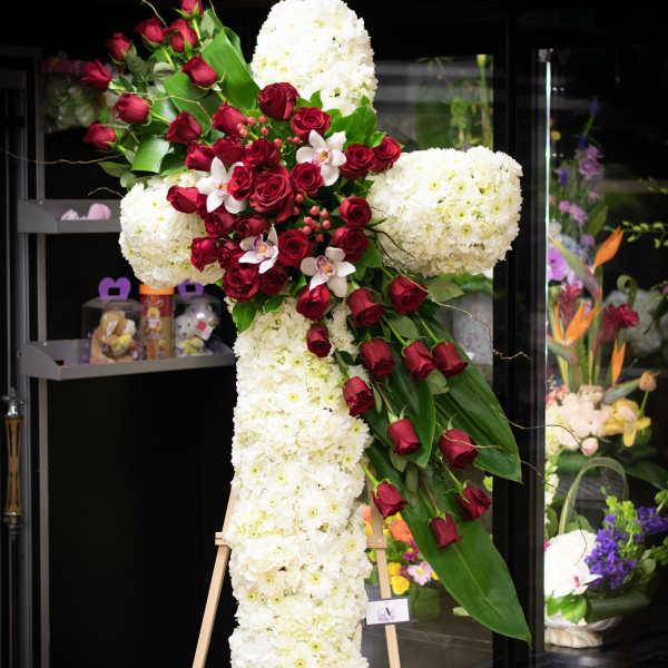 Large cross-shaped floral tribute with white blooms and red roses on an easel