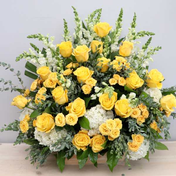 Large arrangement of yellow roses, yellow spray roses, white hydrangeas, and white snapdragons in a wooden container