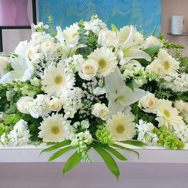 Large white floral arrangement with lilies, roses, and daisies on a table