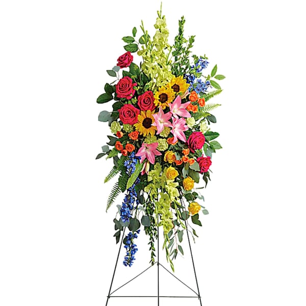 Tall standing floral spray with roses, lilies, sunflowers, and blue accents