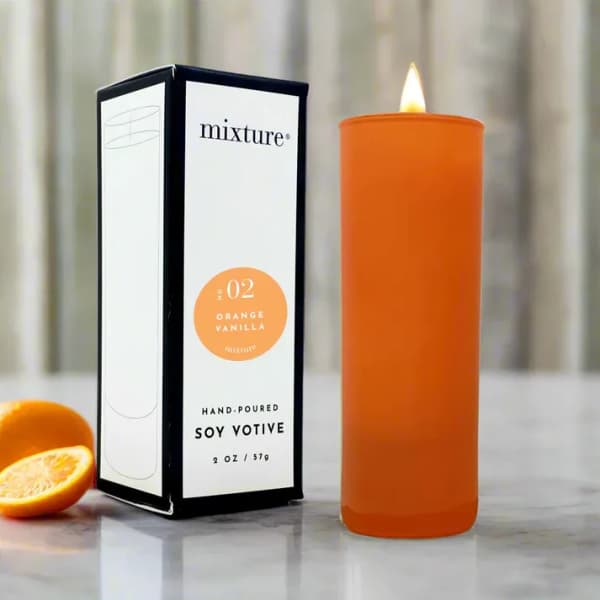 Orange soy votive candle beside its box with orange slices