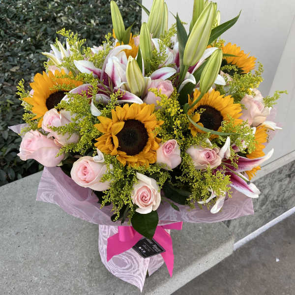 Bouquet of sunflowers, pink roses, and lilies wrapped in pink paper