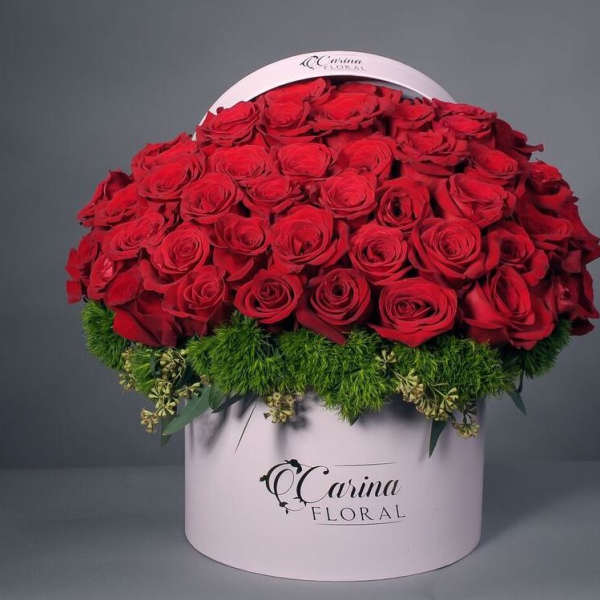 Red roses arranged in a round pink hat box with green filler at the base