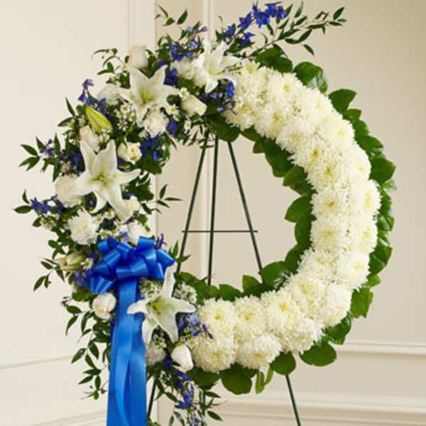 White floral funeral wreath with blue ribbon on an easel