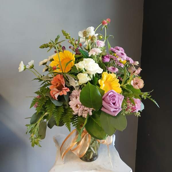 Mixed bouquet of roses, gerbera daisies, and small pink flowers in a glass vase