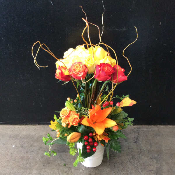 Tall floral arrangement with yellow and red roses in a white vase
