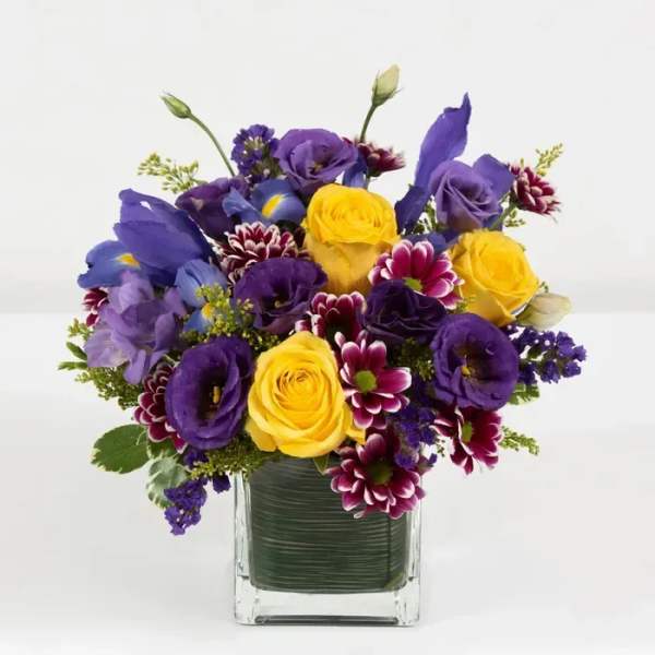 Bouquet of yellow and purple flowers in a clear square vase