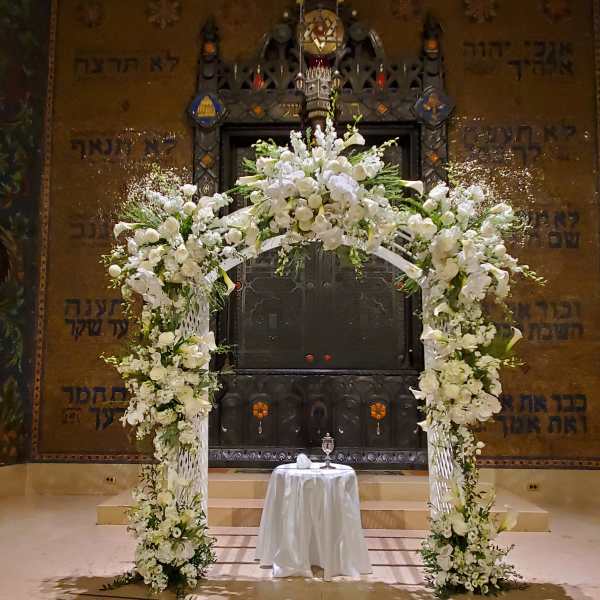 Tall white floral arch with matching column arrangements framing a small draped table