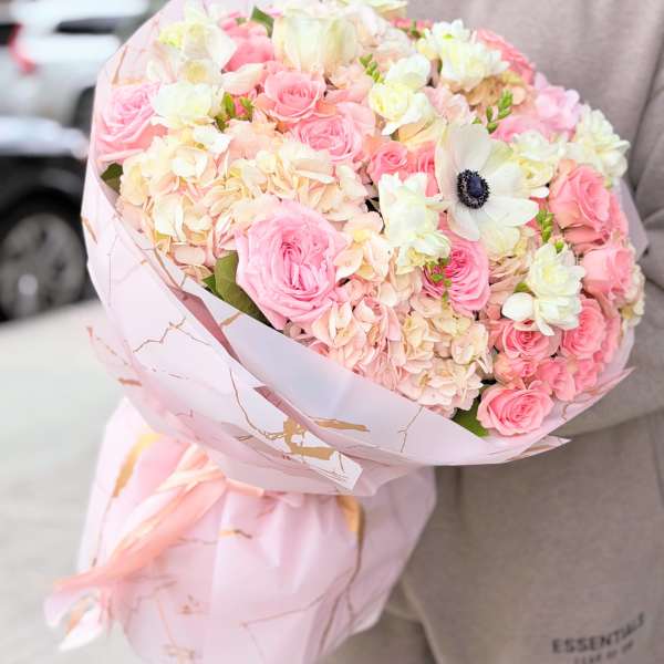 Pink and white bouquet of roses and hydrangeas wrapped in pale pink paper