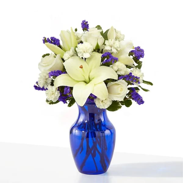 White lilies and roses in a blue glass vase with purple filler flowers