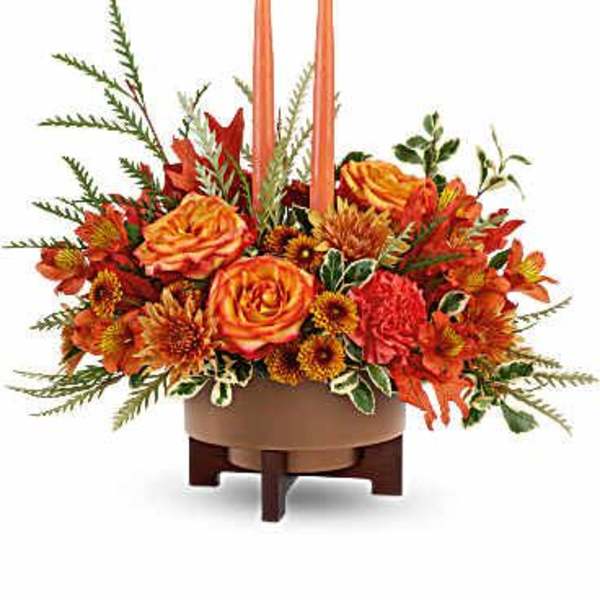Orange floral centerpiece with two tall candles in a low bowl