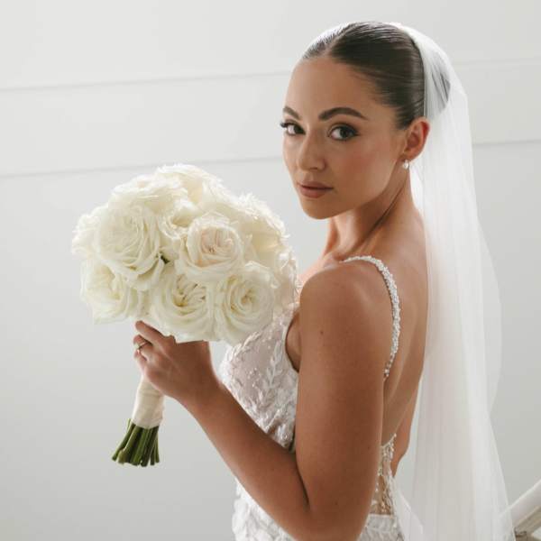 Bride holding a white rose bouquet with a veil and lace gown